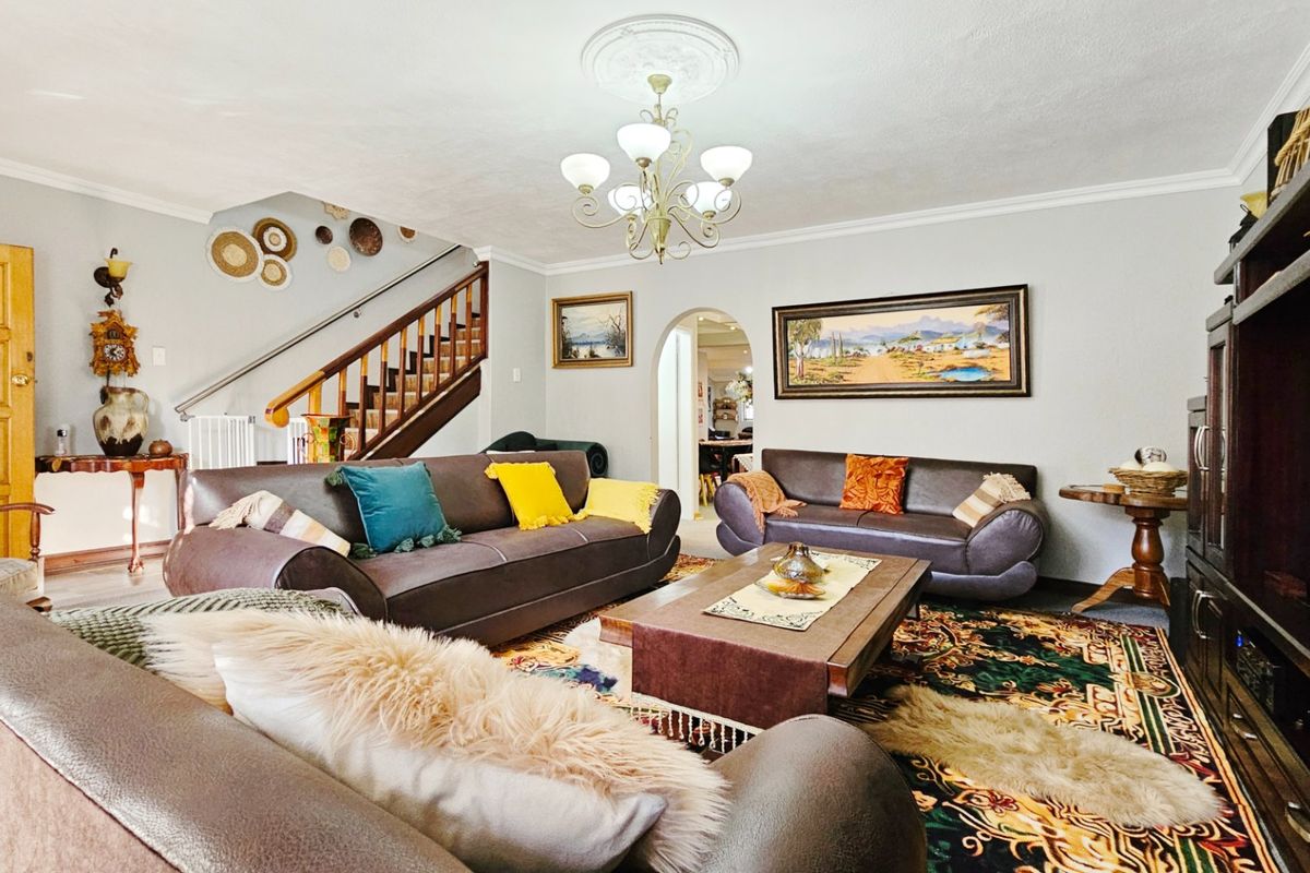 Spacious living room featuring a traditional staircase, decorative ceiling rose, and an arched entryway leading to adjacent living areas.