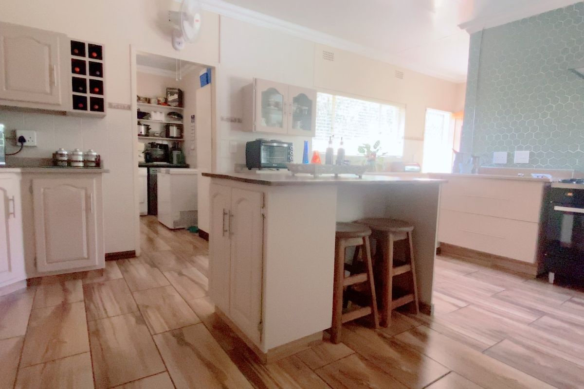 A functional kitchen featuring a central island, built-in cabinetry, a gas stove with extractor fan, and a tiled backsplash, with an adjacent scullery area.