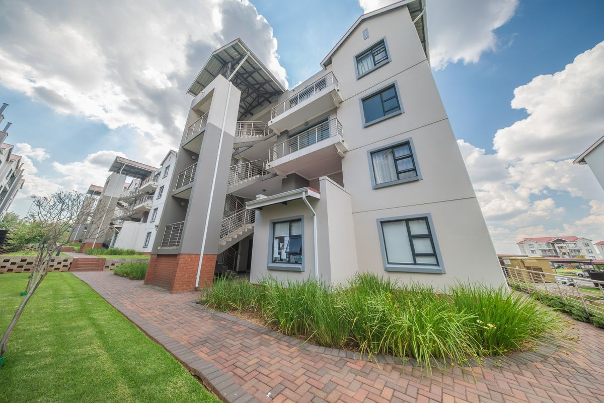 Exterior view of a modern townhouse complex featuring multi-level balconies, metal staircases, and well-maintained brick paved walkways with landscaped garden areas.