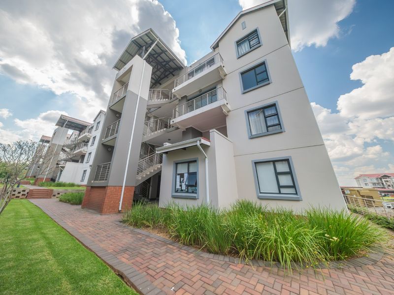Exterior view of a modern townhouse complex featuring multi-level balconies, metal staircases, and well-maintained brick paved walkways with landscaped garden areas.