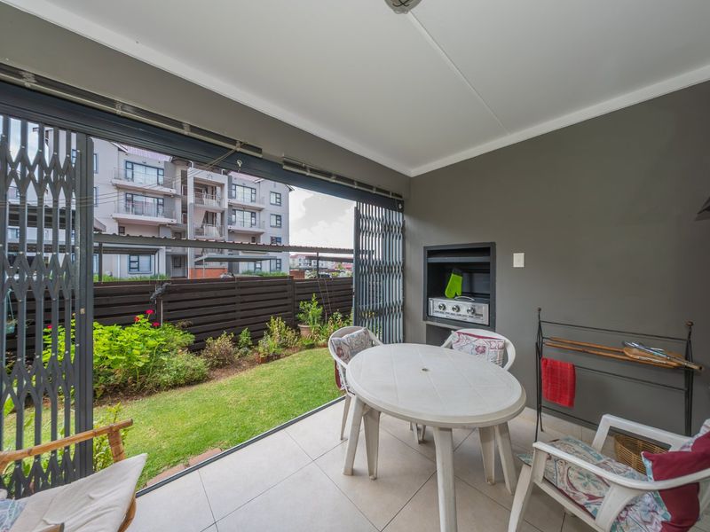 Covered patio area featuring a built-in braai, tiled flooring, and direct access to a small private garden through retractable security gates.