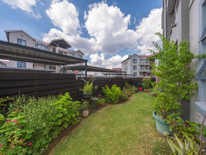 A well-maintained rear garden area featuring a manicured lawn, established garden beds, and timber slat fencing, adjacent to a residential carport structure.