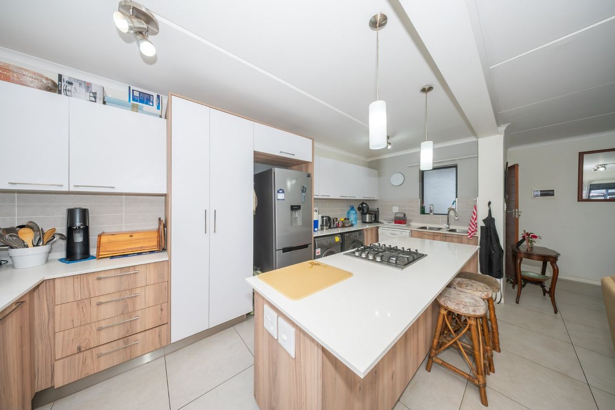 Modern kitchen featuring a central island with a gas cooktop, stone countertops, ample built-in cabinetry, and tiled flooring throughout.