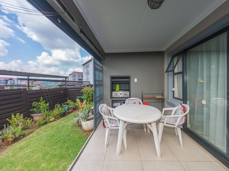 Covered patio featuring tiled flooring, a built-in braai, and direct access to a private garden area through sliding glass doors.