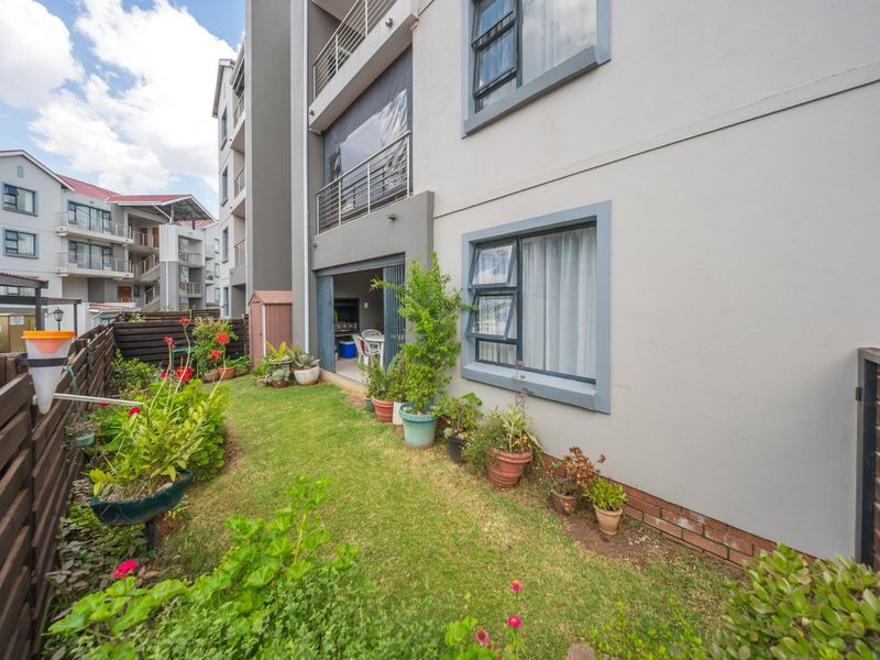 Rear view of the townhouse featuring a small private garden, lawn area, timber fencing, and access to a ground-floor patio and upper-level balcony.