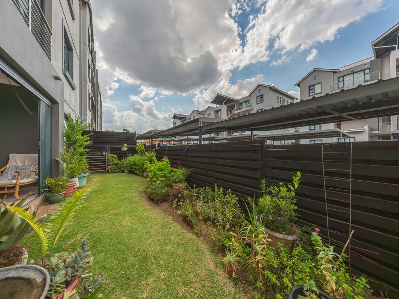 A private rear garden area featuring a well-maintained lawn, timber slat fencing, and direct access to the townhouse interior via sliding glass doors.