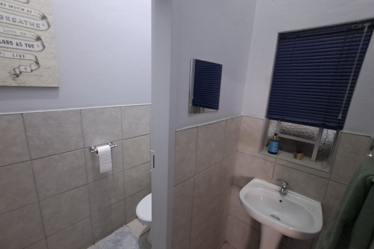 A functional bathroom featuring a pedestal basin, tiled walls, and a separate toilet area with a privacy partition.