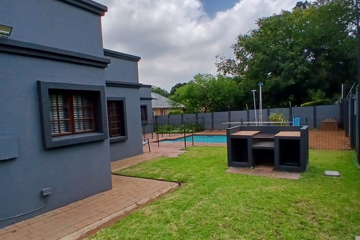 Rear garden featuring a paved patio, built-in braai area, and a swimming pool enclosed by perimeter fencing.