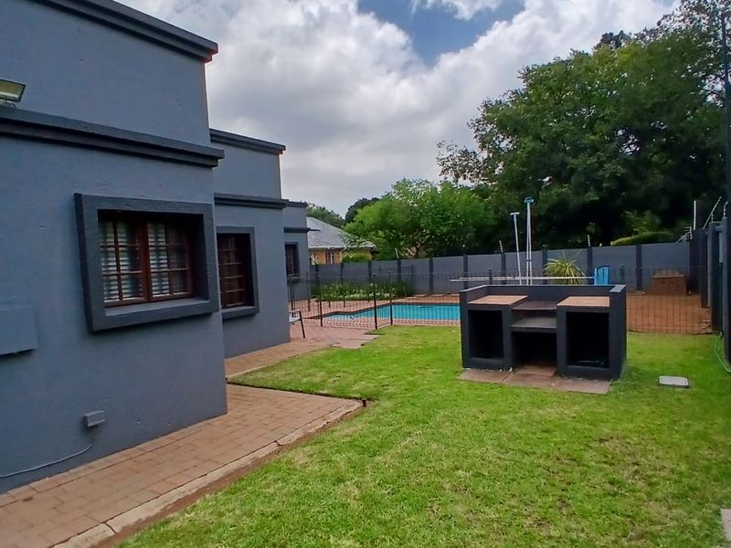 Rear garden featuring a paved patio, built-in braai area, and a swimming pool enclosed by perimeter fencing.