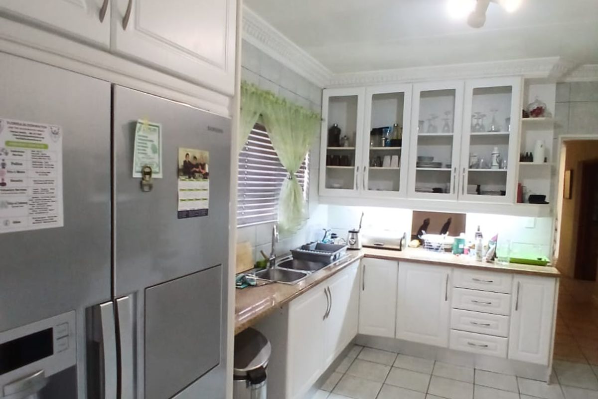 A functional kitchen featuring white cabinetry, glass-fronted display units, double sink, and tiled flooring with decorative inlay.