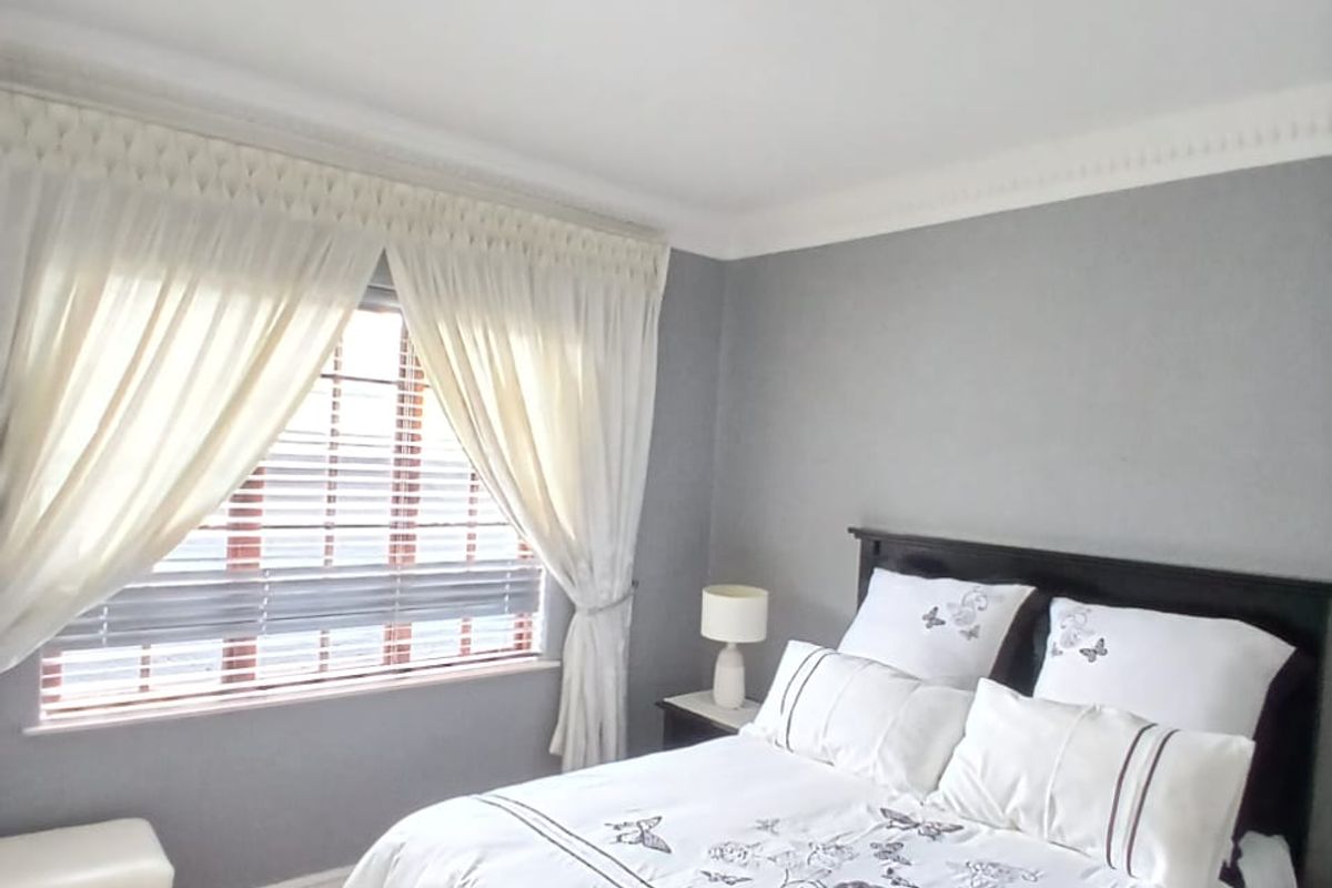 A well-maintained bedroom featuring crown molding, neutral grey walls, and a window fitted with venetian blinds and curtains.