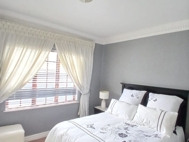 A well-maintained bedroom featuring crown molding, neutral grey walls, and a window fitted with venetian blinds and curtains.