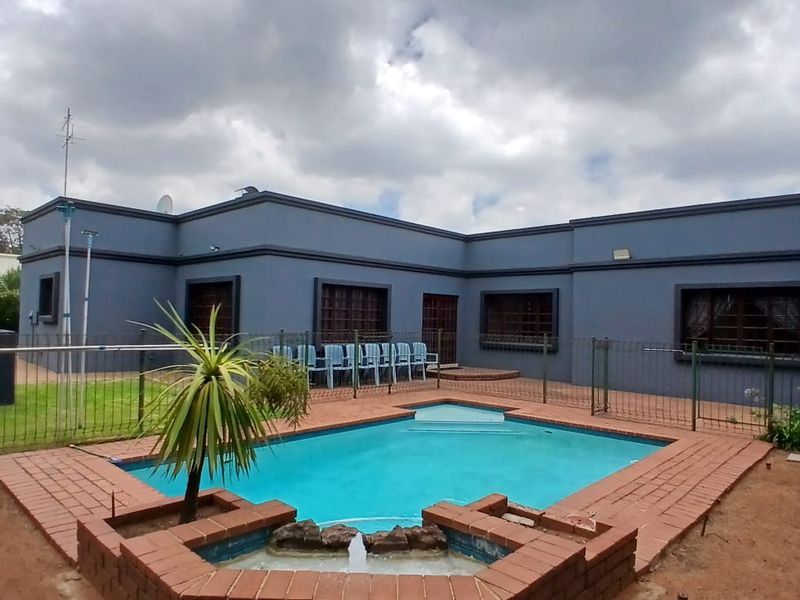Rear exterior view featuring a swimming pool with a brick water feature, surrounded by metal fencing and a painted exterior facade.