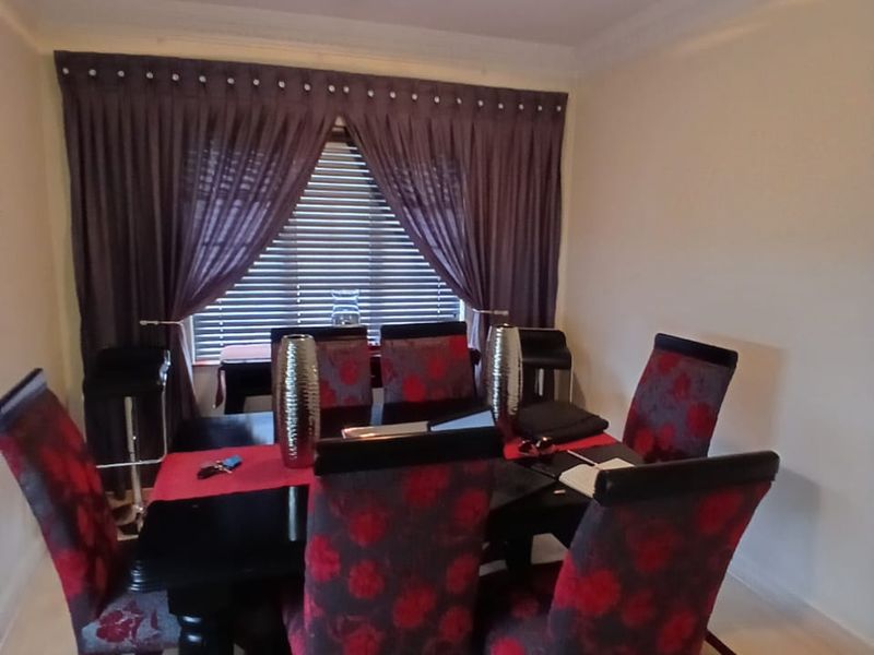 A dining room featuring coved cornicing, a central ceiling light fixture, and a window fitted with venetian blinds and decorative curtains.