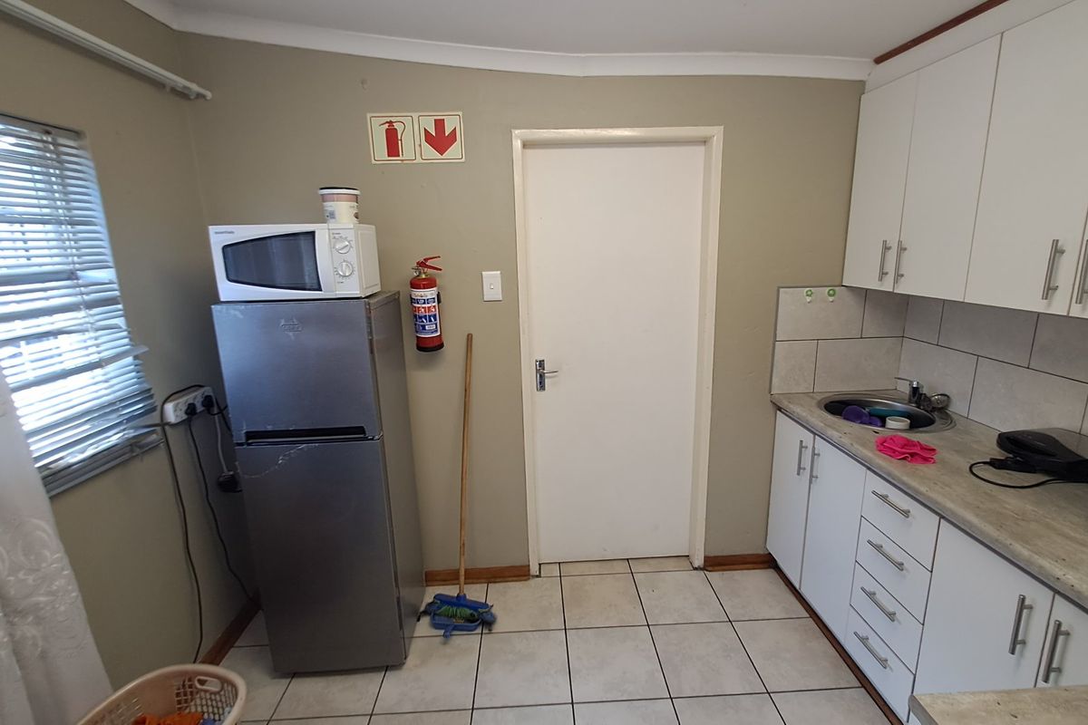 A functional kitchen featuring white cabinetry, laminate countertops, a stainless steel sink, and tiled flooring, providing a practical workspace.