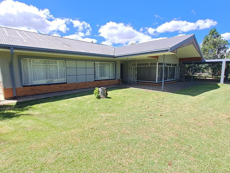 A rear view of a single-story house featuring a corrugated metal roof, brick accents, a covered patio area, and an attached carport.