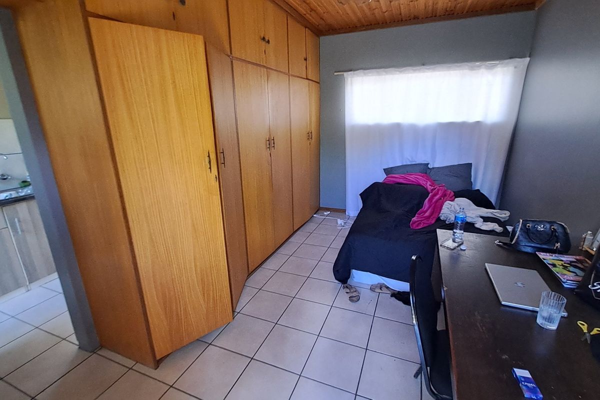 Bedroom featuring built-in wooden cupboards, tiled flooring, and a timber ceiling, with an adjacent view into a kitchen area.