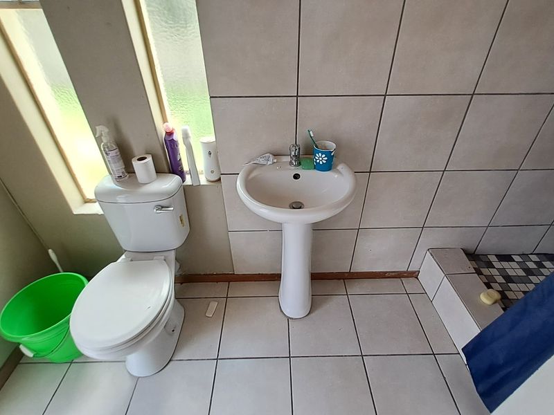 A functional bathroom featuring a pedestal basin, toilet, and tiled shower area with neutral wall and floor tiling.