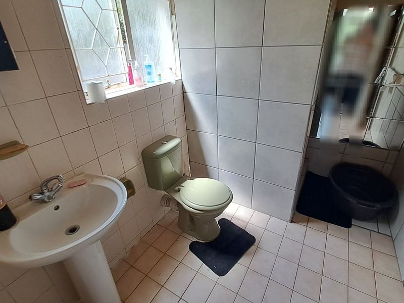 A dated bathroom featuring a pedestal basin, toilet, and full-height ceramic wall tiling with a leaded glass window.
