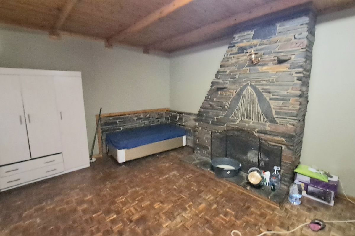 Living room featuring a prominent stone fireplace, exposed timber beam ceiling, and parquet flooring, offering a rustic aesthetic with potential for modernization.