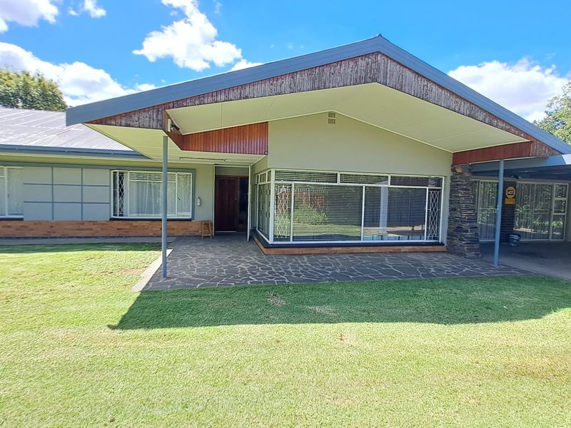 Front elevation of a single-story house featuring a stone-clad pillar, timber-accented roofline, paved patio area, and an attached carport.