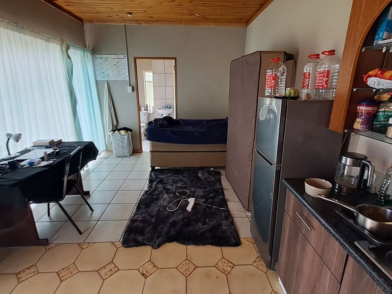 Open-plan living area featuring tiled flooring, timber ceiling, and a compact kitchen kitchenette, with direct access to an adjoining bathroom.