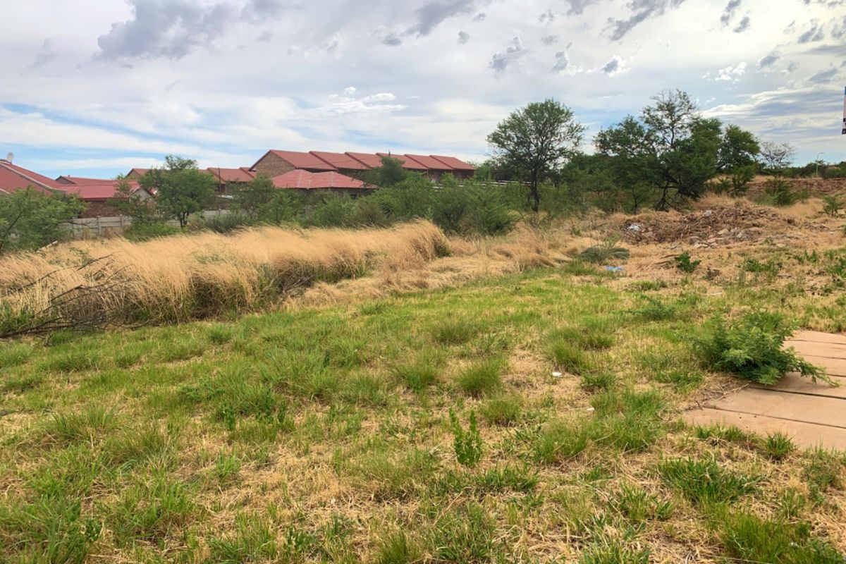 A view of a vacant residential plot featuring natural grassland and scattered trees, suitable for future development.