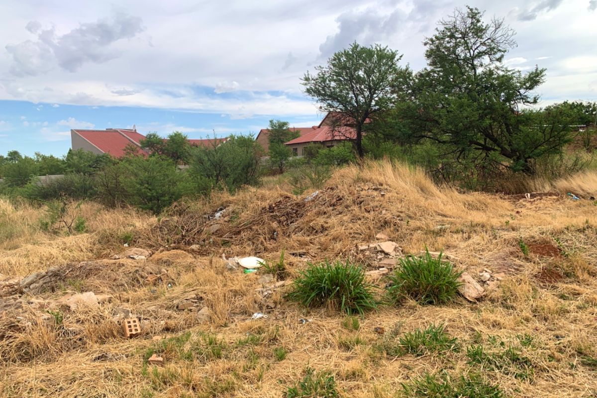 A view of the vacant residential land featuring overgrown grass, scattered debris, and mature trees on the property.