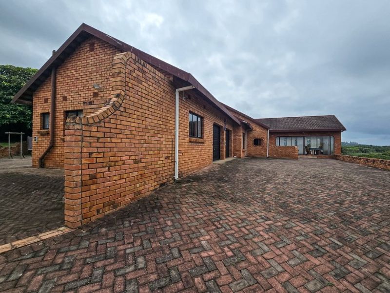 A view of the front exterior featuring a face-brick facade, extensive paved driveway, and a tiled roof structure.