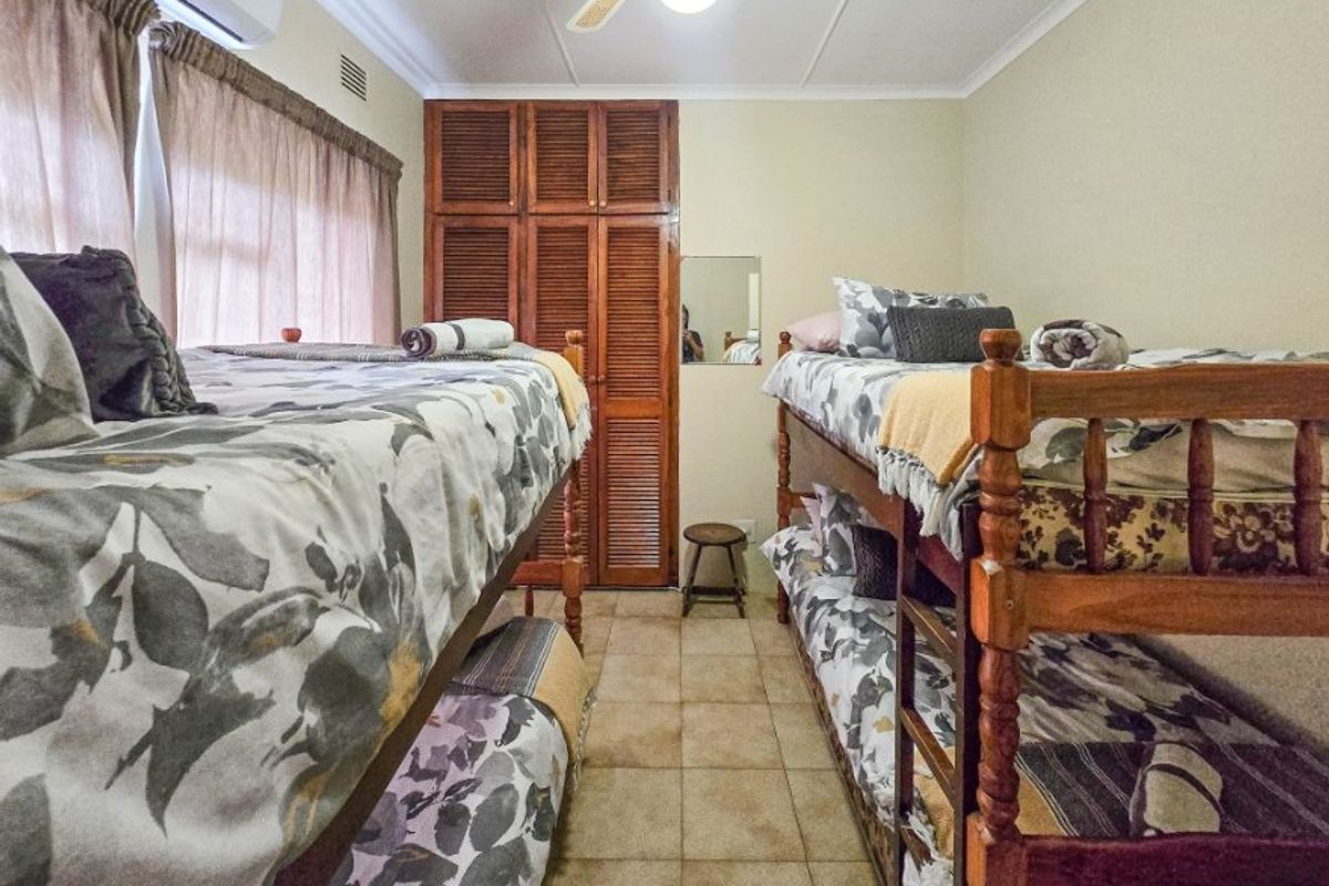 A functional bedroom featuring tiled flooring, built-in wooden cupboards, a ceiling fan, and an air conditioning unit.