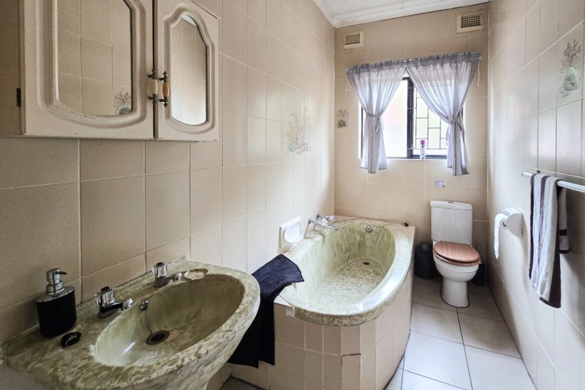 A dated bathroom featuring a pedestal basin, built-in bathtub, and toilet with full-height wall tiling and tiled flooring.