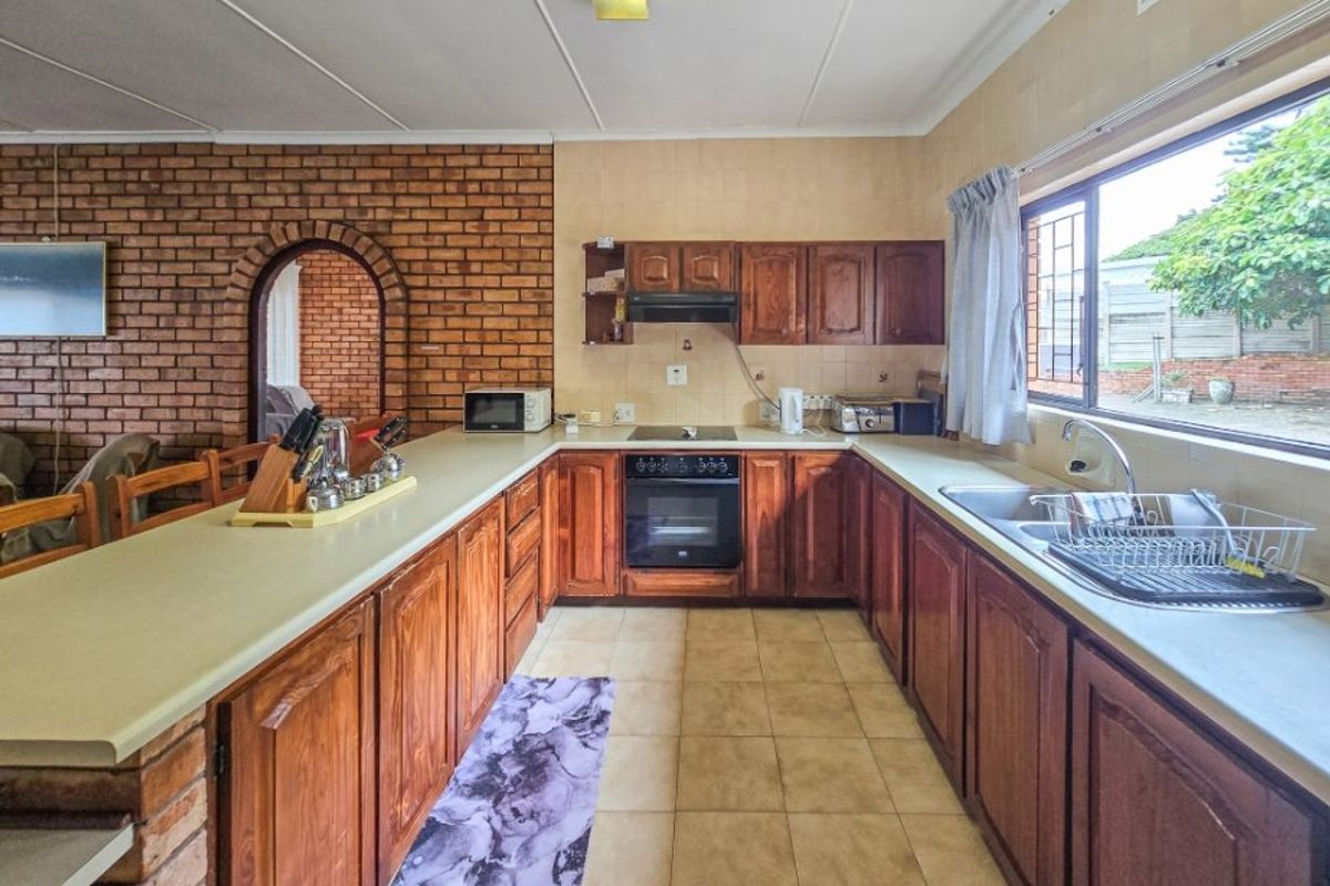 Spacious kitchen featuring traditional wooden cabinetry, an exposed brick feature wall, built-in oven and hob, and a functional layout with ample counter space.