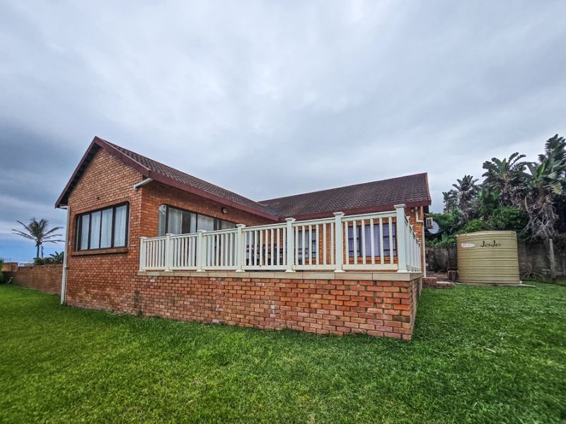 Rear view of a brick house featuring a raised patio with white balustrades and an integrated water storage tank in the garden.