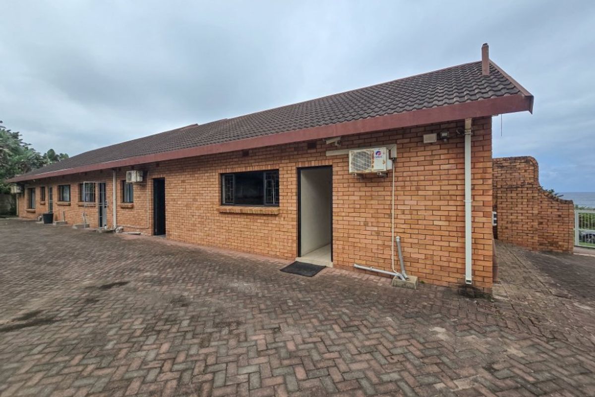 A rear view of a face brick house featuring a paved courtyard, tiled roof, and exterior air conditioning units.