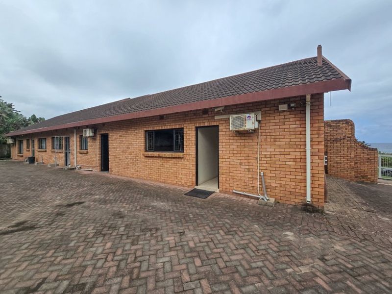 A rear view of a face brick house featuring a paved courtyard, tiled roof, and exterior air conditioning units.