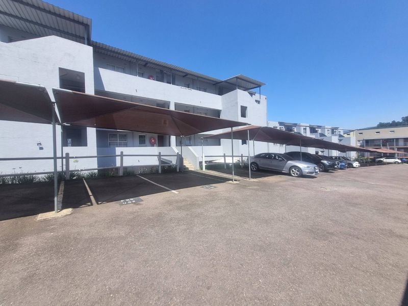Exterior view of an apartment complex featuring a paved parking area with covered shade cloth carports and building access stairs.