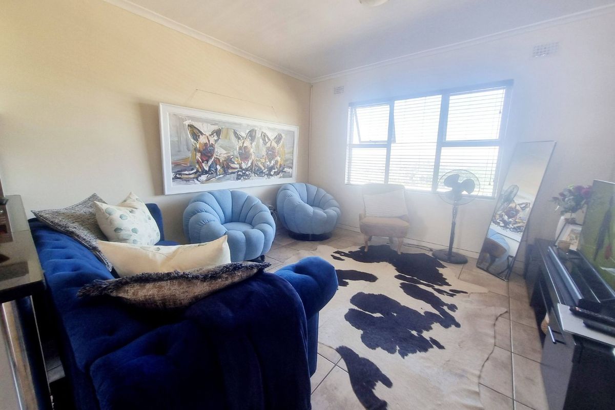 A living room featuring tiled flooring, large windows with venetian blinds, and neutral wall finishes, providing a functional and well-lit space.