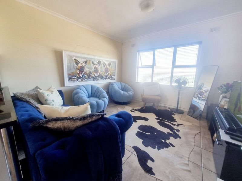 A living room featuring tiled flooring, large windows with venetian blinds, and neutral wall finishes, providing a functional and well-lit space.