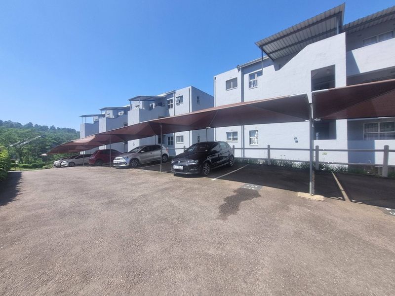 Exterior view of an apartment complex featuring covered parking bays and a paved driveway area.