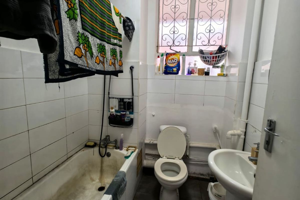 A compact bathroom featuring a bathtub, pedestal sink, and toilet, with a window providing natural light and security bars.