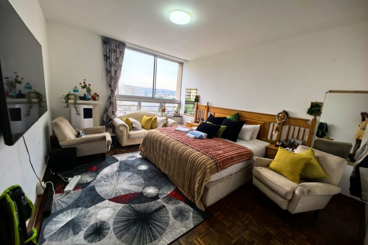 Spacious bedroom featuring parquet flooring, large windows with city views, and ample natural light.