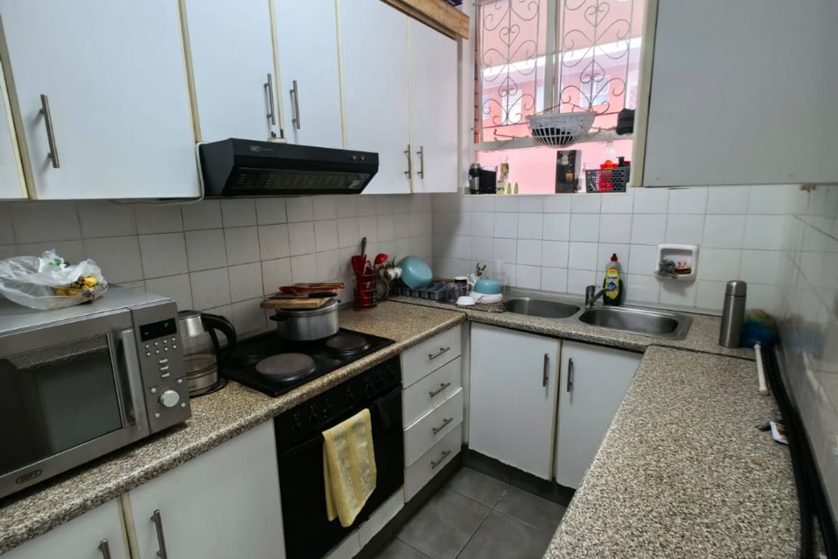 A compact kitchen featuring white cabinetry, granite-look countertops, a built-in oven with hob, extractor fan, and a double stainless steel sink.