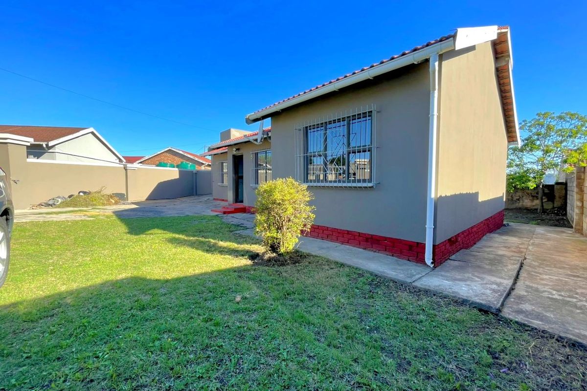 Rear view of the house featuring a lawn, concrete pathways, security bars on windows, and a perimeter wall.