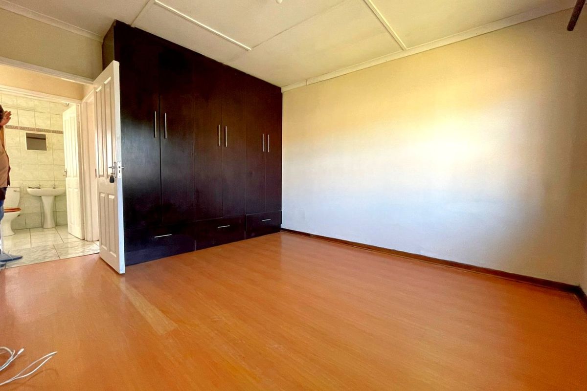 A vacant bedroom featuring dark built-in cupboards, laminate flooring, and a tiled ceiling, with an adjacent view into a tiled bathroom.
