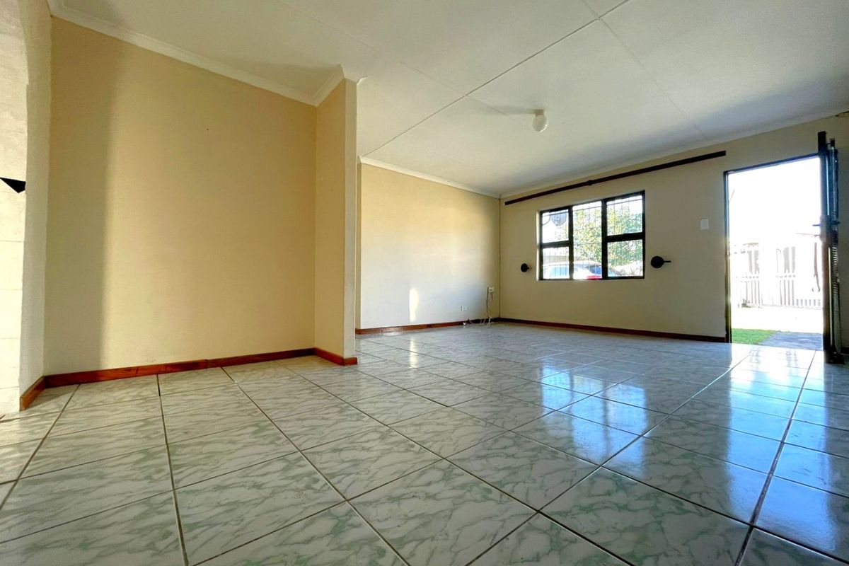 An empty, open-plan living area featuring ceramic floor tiles, security bars on windows, and a direct exterior access point.