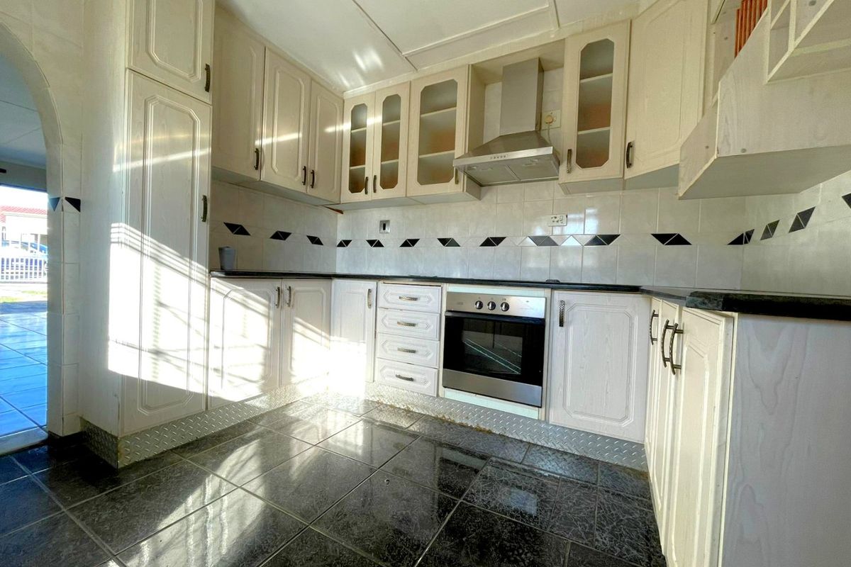 A functional kitchen featuring built-in cabinetry, a stainless steel oven, extractor fan, and dark tiled flooring with a decorative backsplash.
