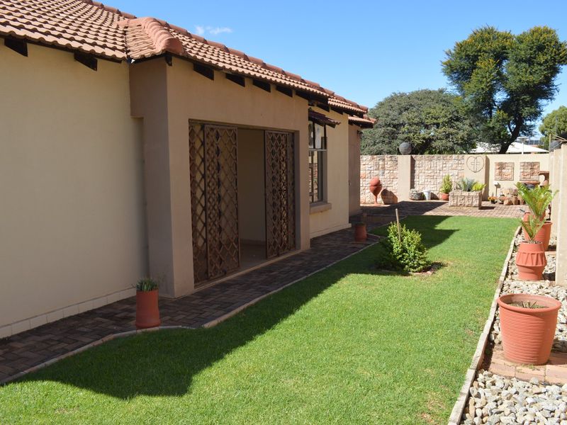 A well-maintained rear garden featuring a paved walkway, lawn, and secure access to the townhouse interior via metal security gates.