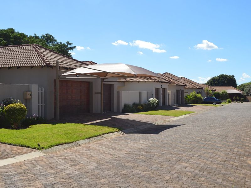 A street-level view of a residential townhouse complex featuring paved driveways, tiled roofs, and covered parking areas.