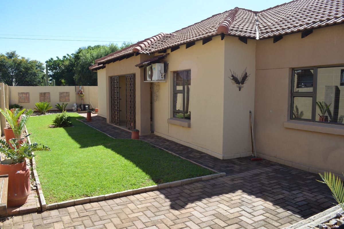 Rear view of the townhouse featuring a paved patio area, a well-maintained lawn, and a secure boundary wall.