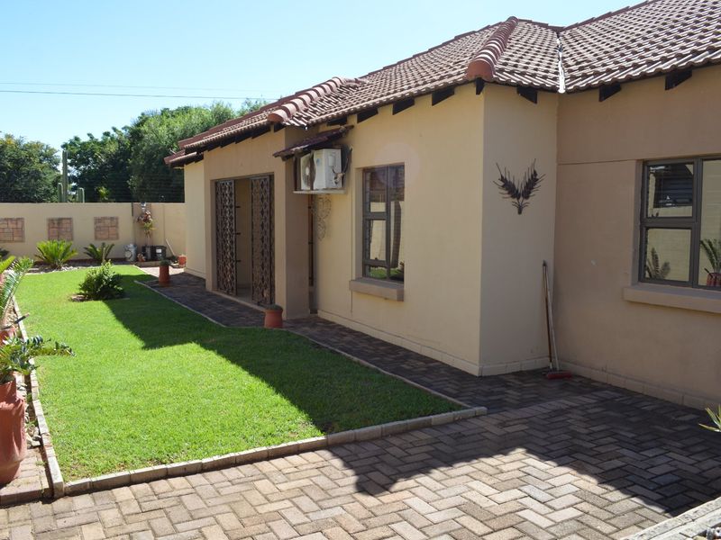 Rear view of the townhouse featuring a paved patio area, a well-maintained lawn, and a secure boundary wall.